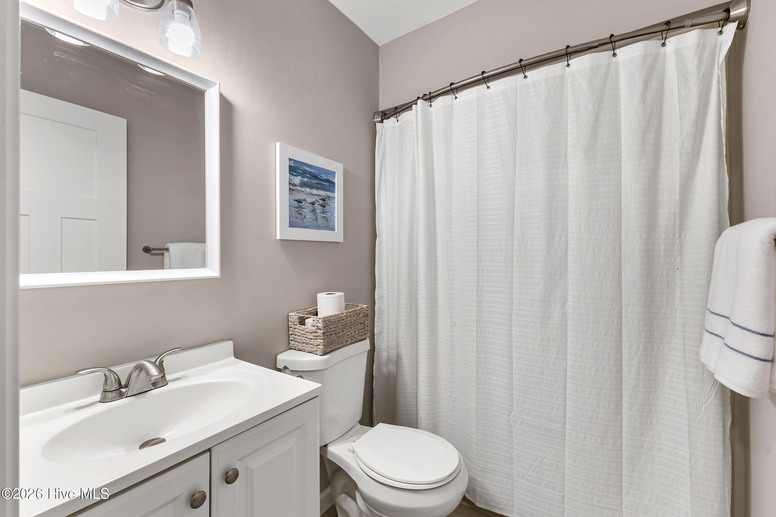 Bathroom with a white vanity, toilet, large mirror, and full-length white shower curtain.