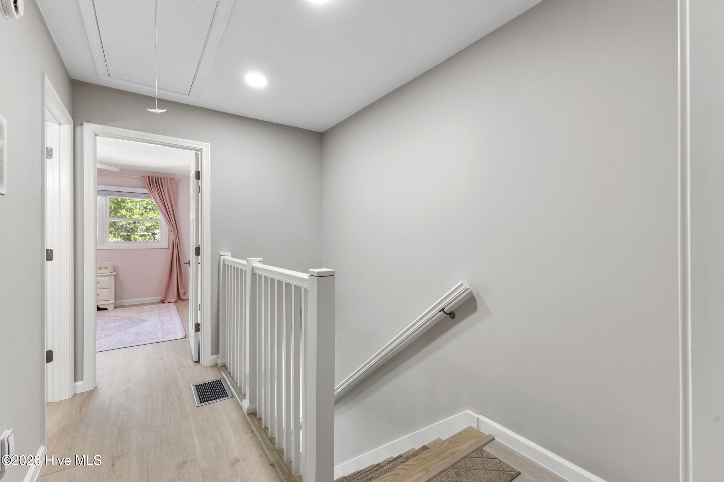 Upstairs stair landing with white railing and an open doorway to a pink bedroom.