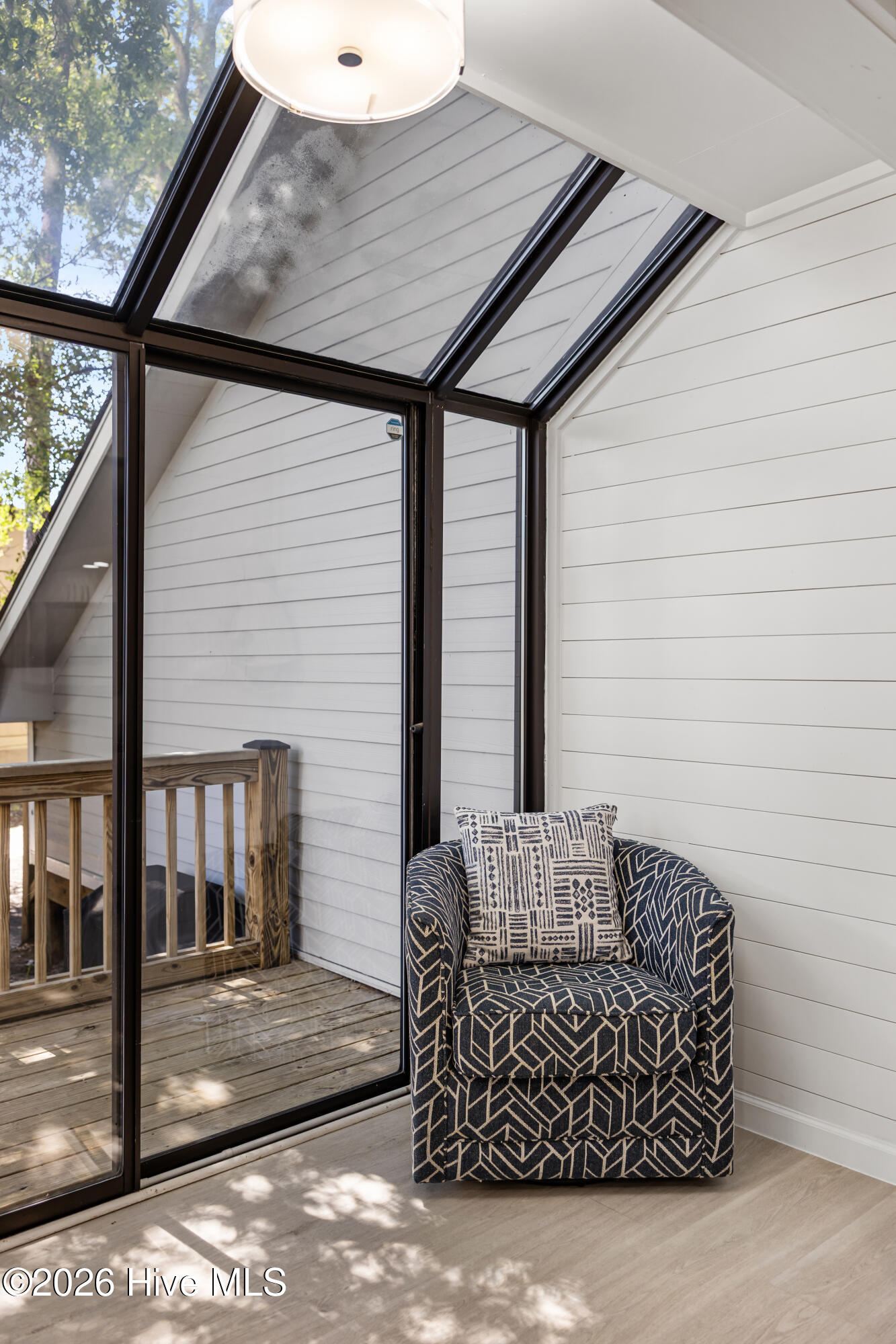 Furnished sunroom with a patterned armchair beside black-framed glass doors opening onto a wooden deck.