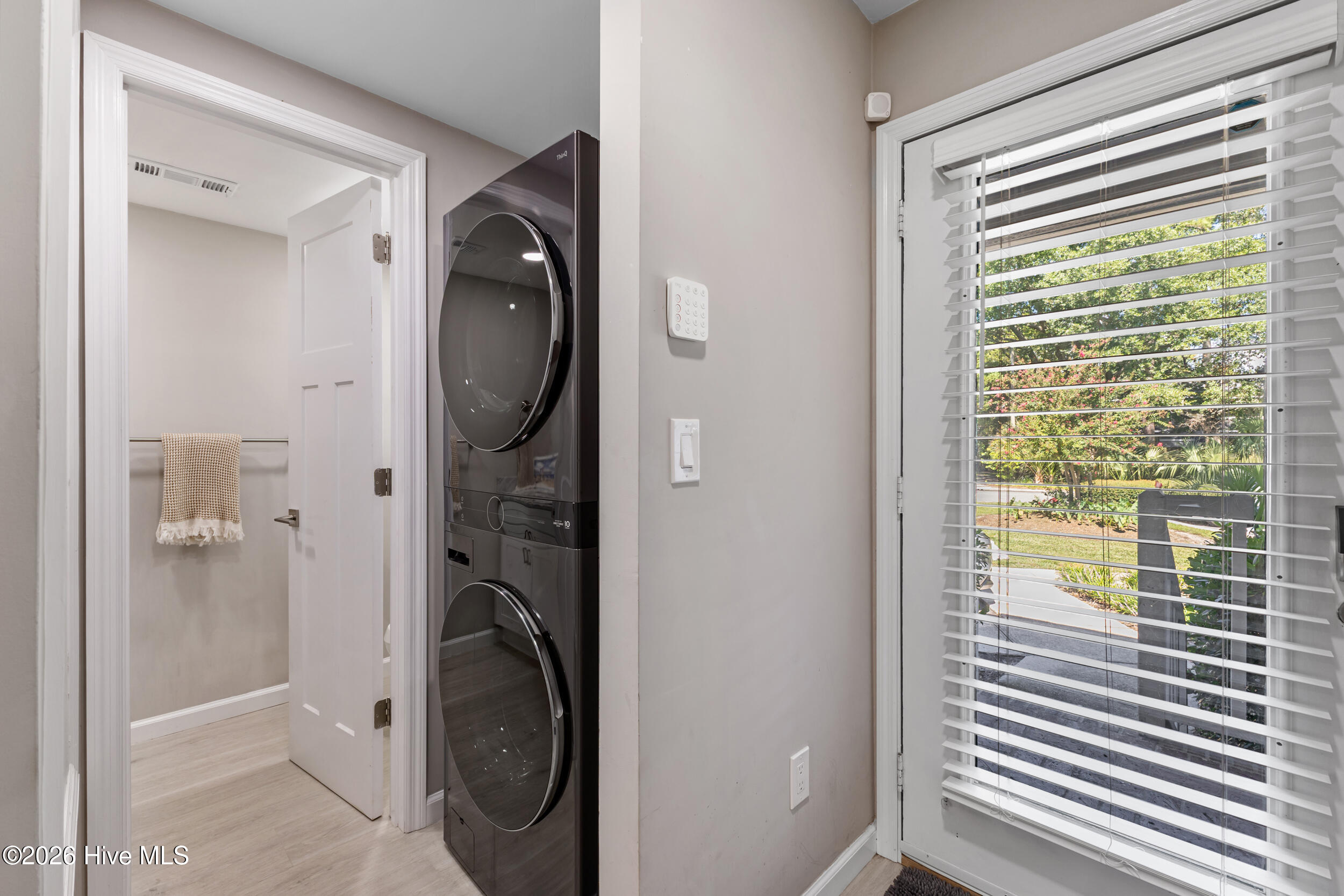 Laundry area with a dark stacked washer and dryer beside a window overlooking greenery.
