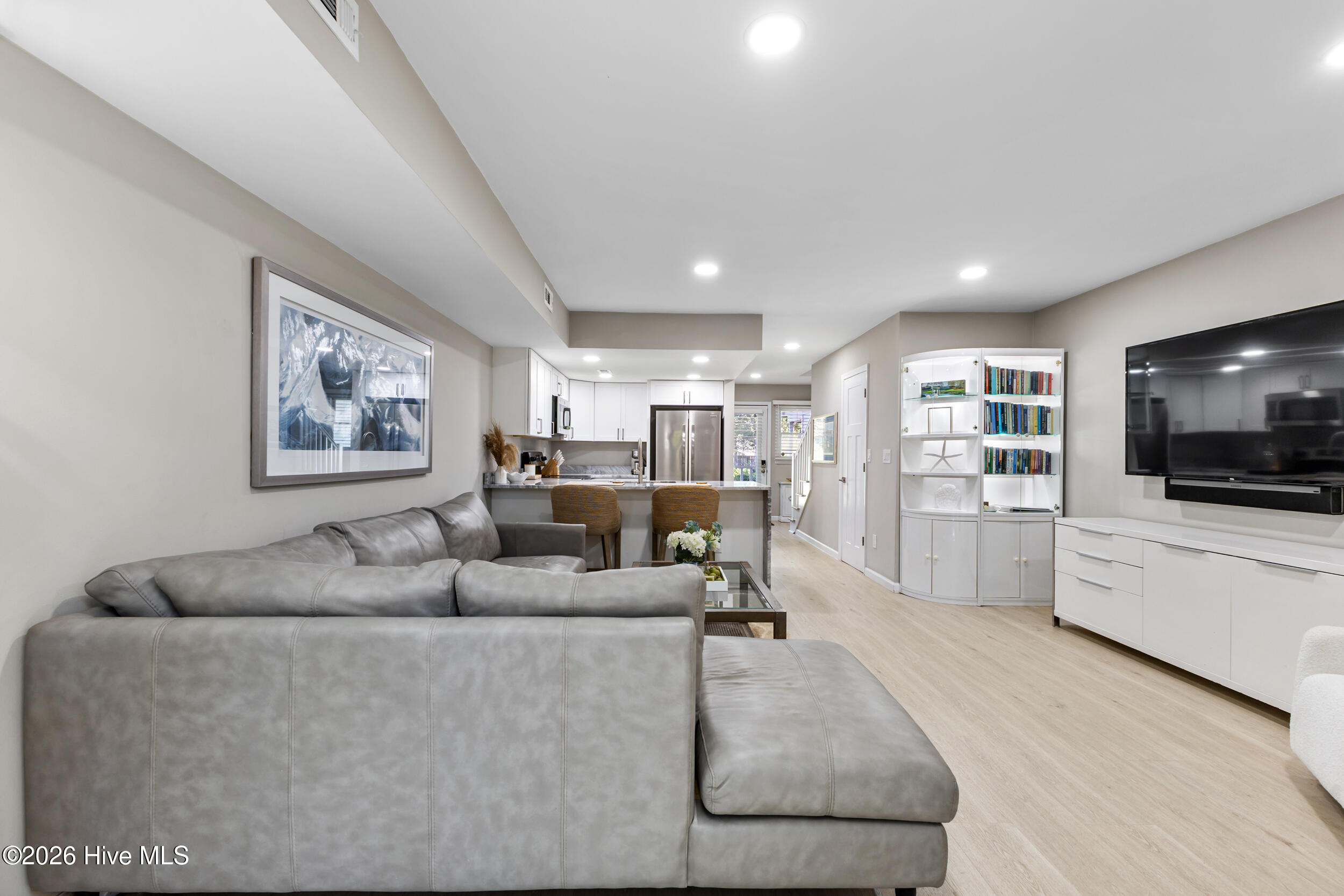 Open-plan living room and kitchen with a gray sectional, white cabinetry, and breakfast bar.