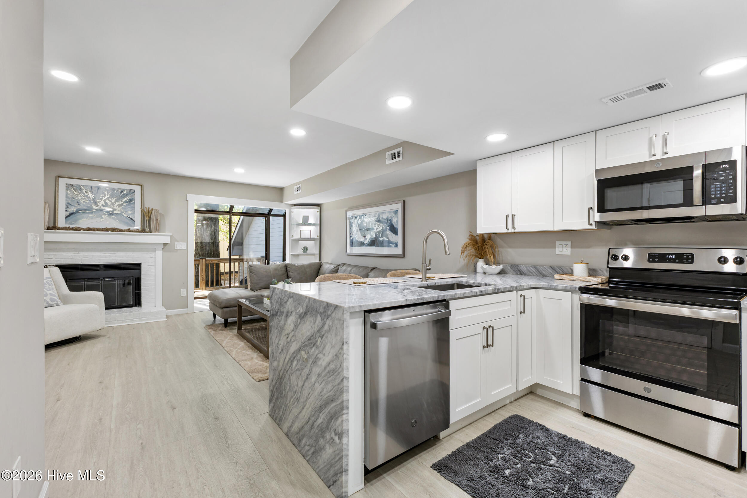 Open-plan kitchen with a marble island, stainless steel appliances, and living area with fireplace.