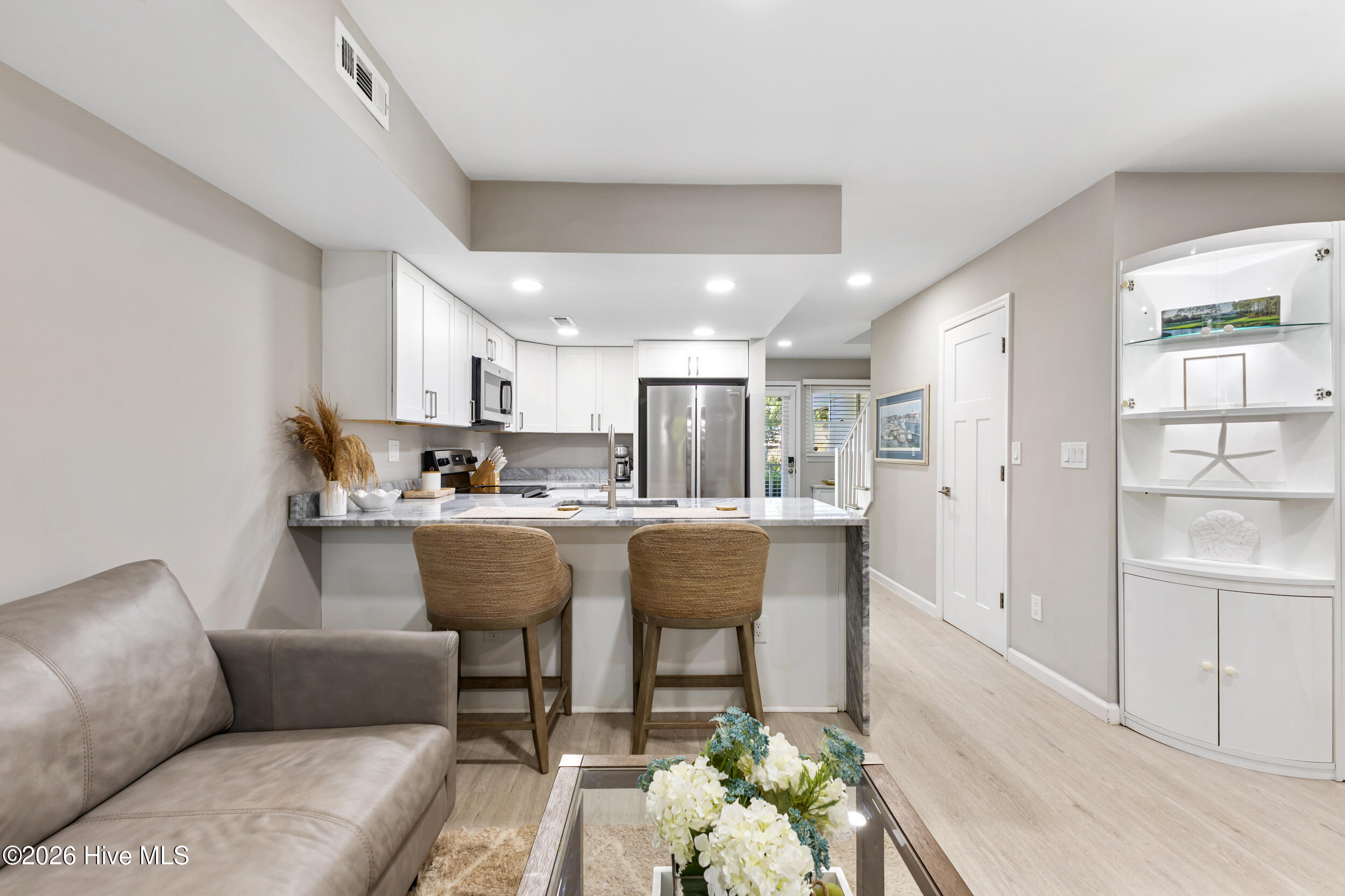 Condo kitchen and living area with a marble-look island, two stools, and gray sofa.