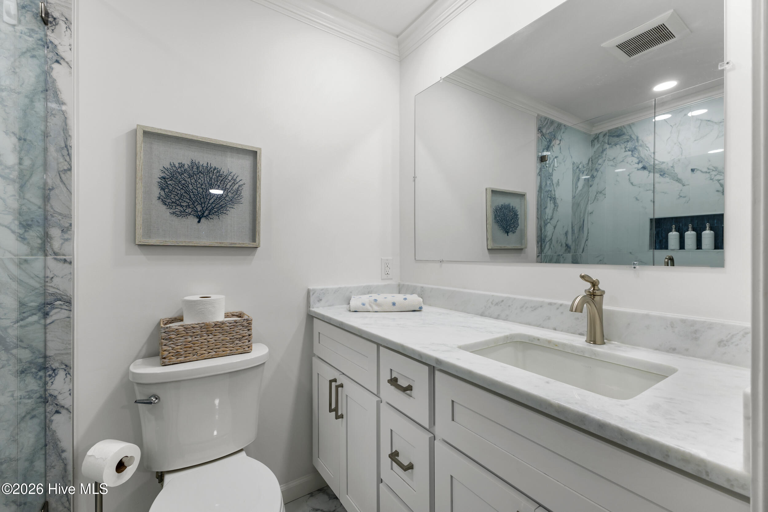 Bathroom with a marble shower, white vanity, brass faucet, and framed coral artwork.