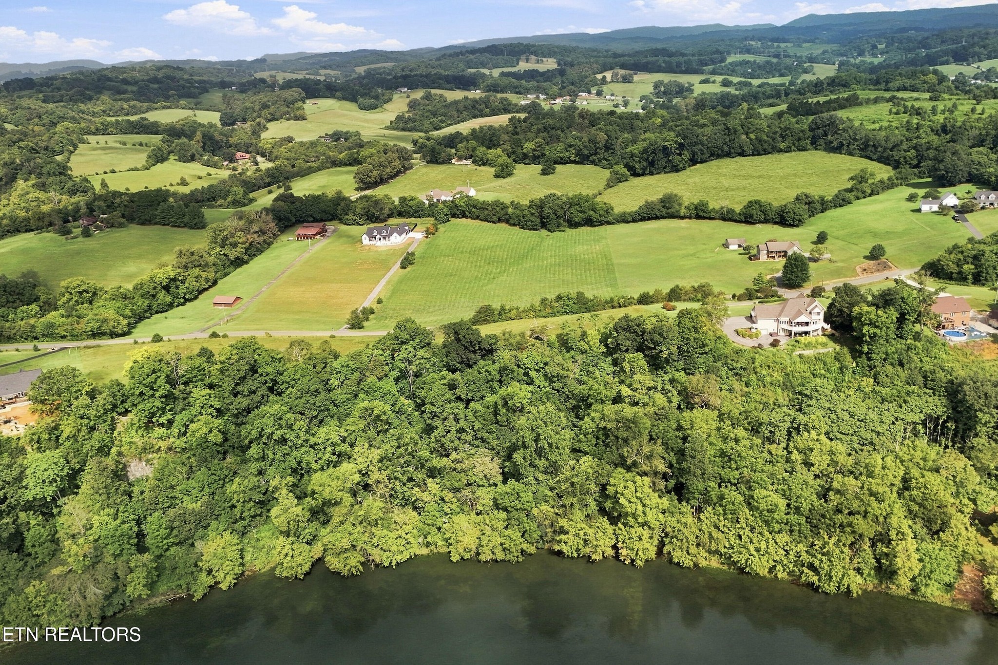 Aerial view of wooded riverfront land, with open fields and rolling hills beyond.