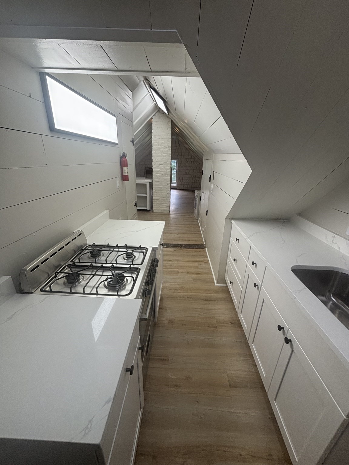 Narrow attic kitchen with white cabinets, a gas range, and sloped ceilings with skylights.