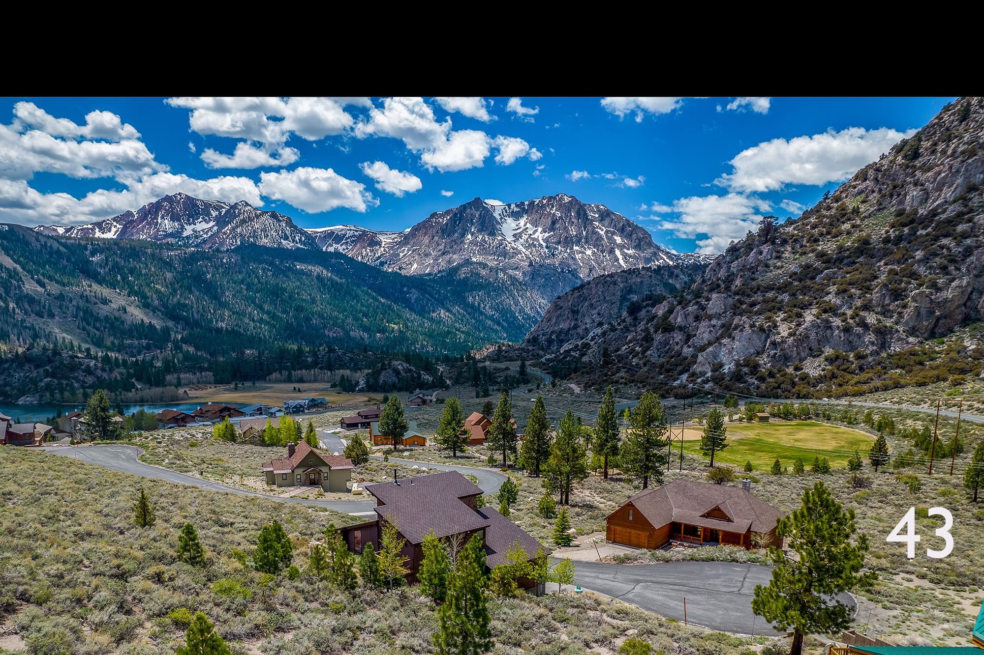 Aerial view of a cabin with a lake and snow-streaked mountains in the background.