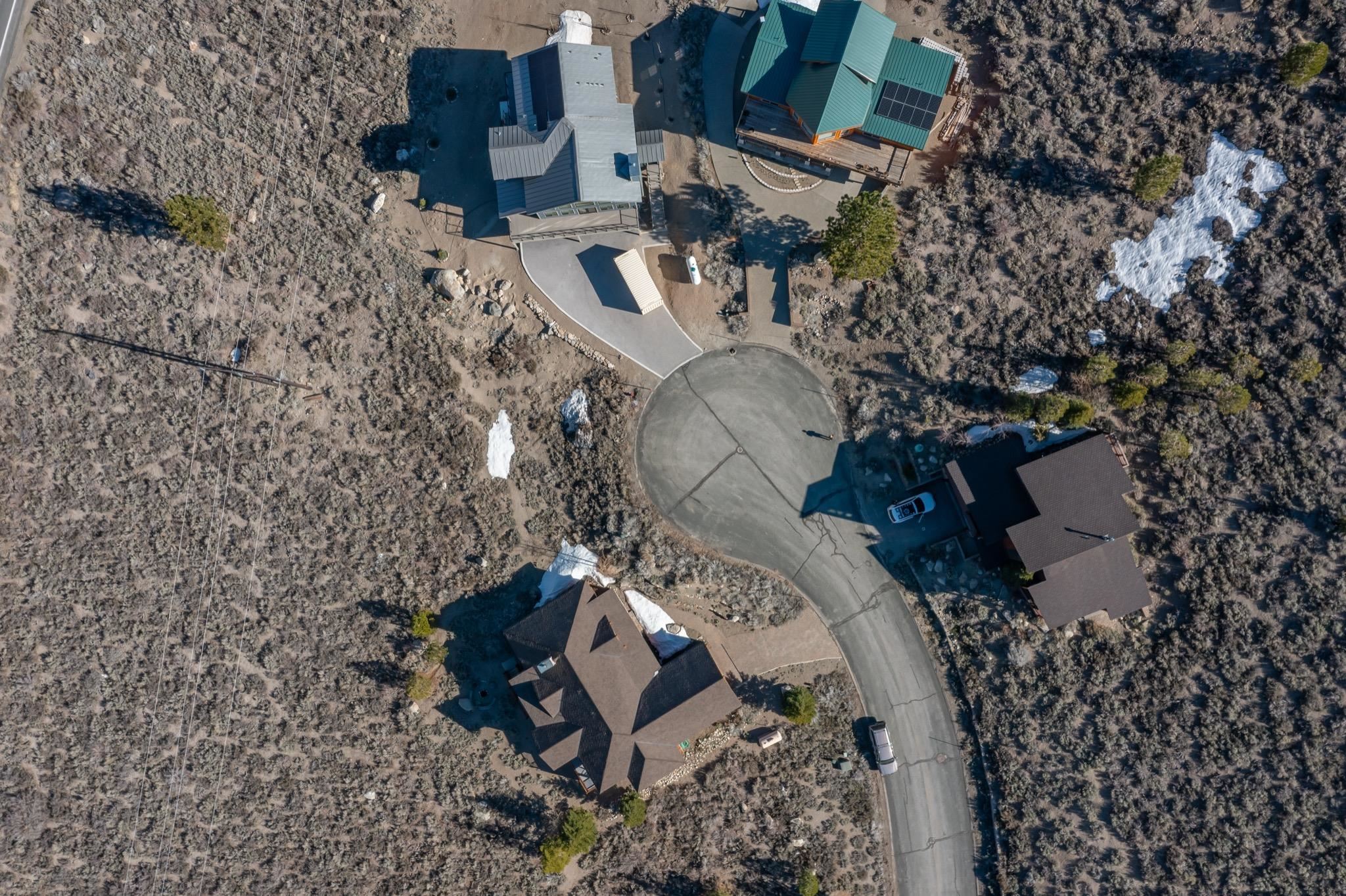 Aerial view of homes beside a curved road and circular turnaround, surrounded by sparse woodland and patches of snow.