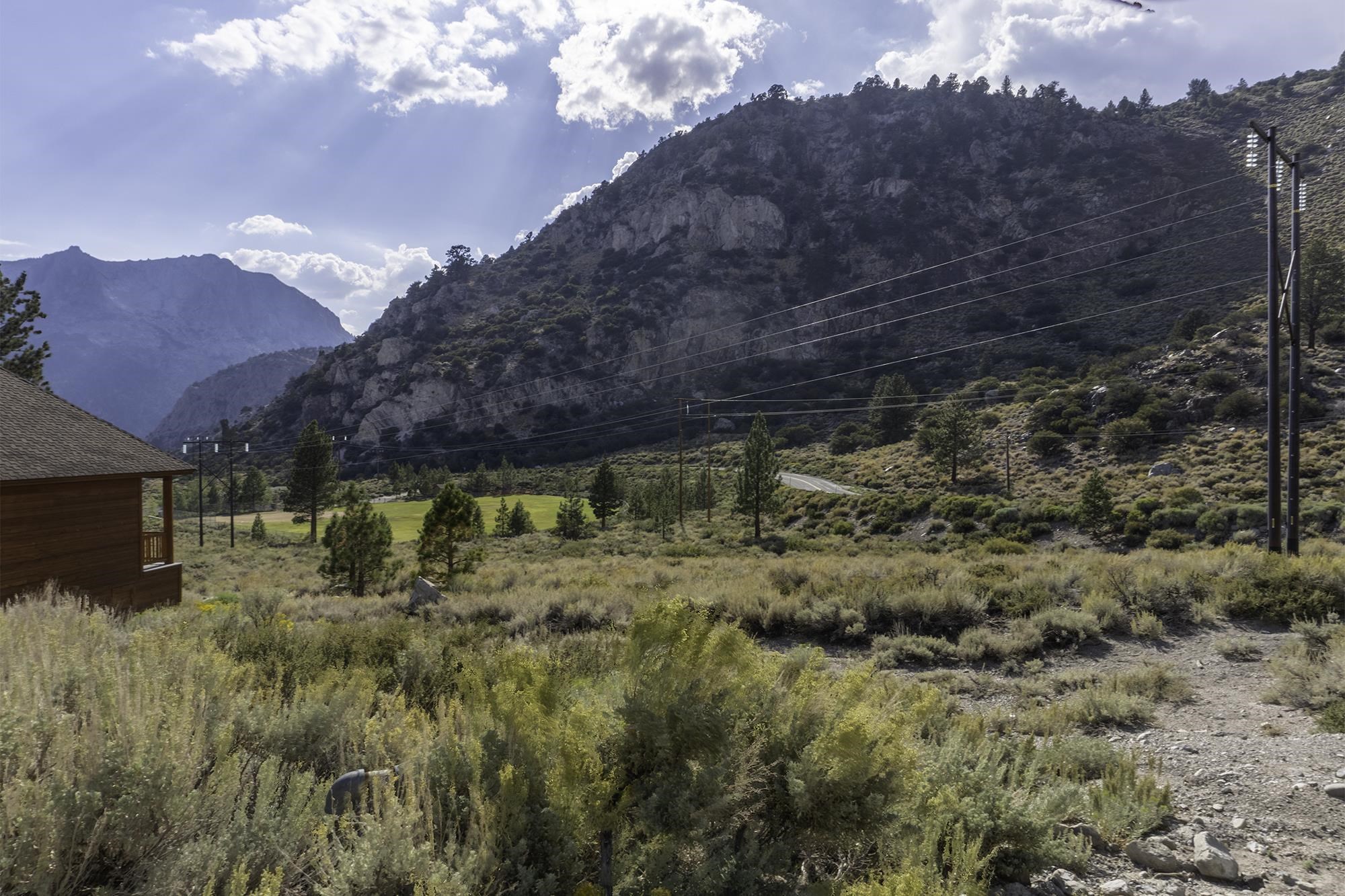 Rocky mountain views beyond a sagebrush lot, with a wooden cabin at the edge.