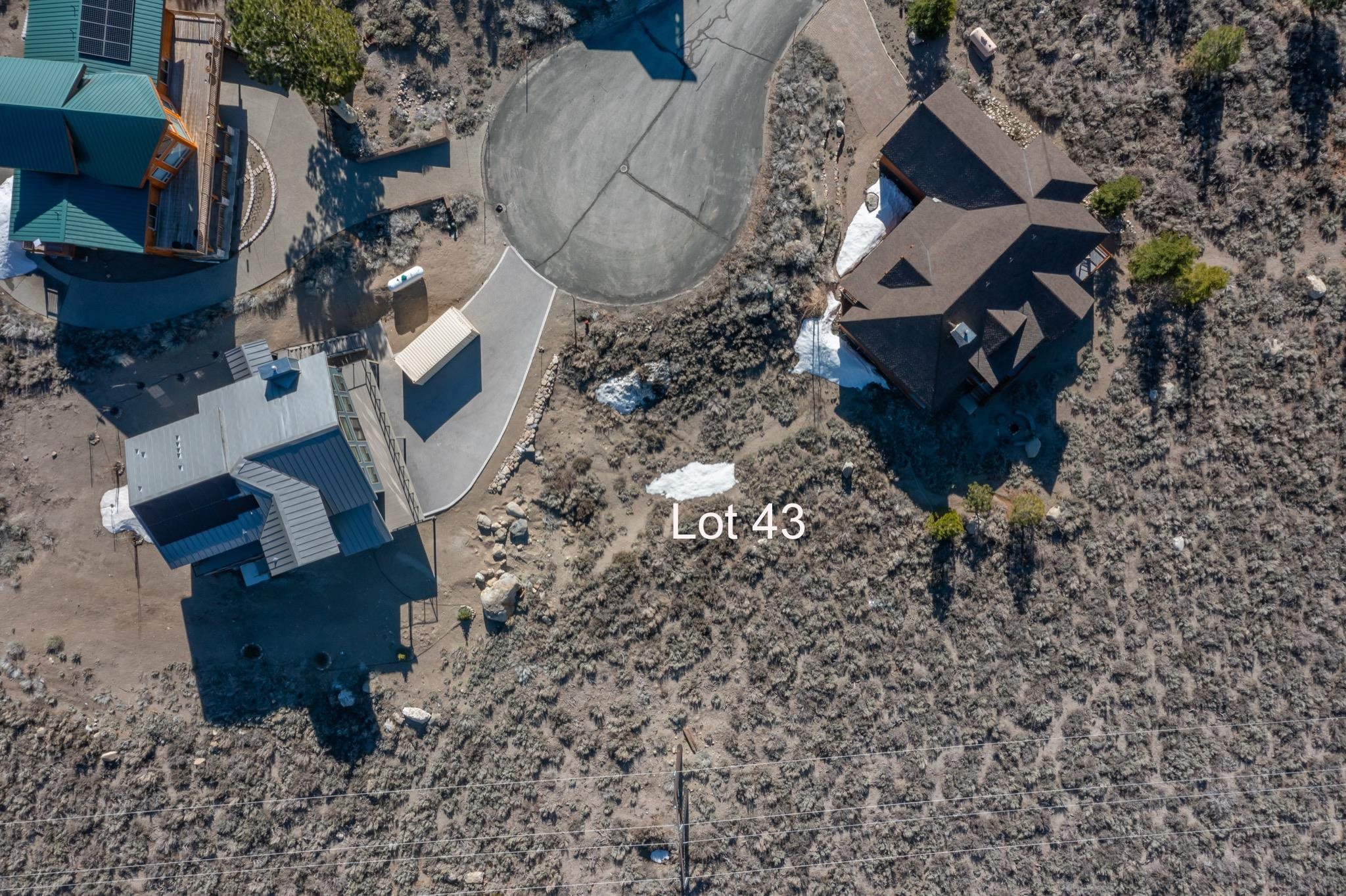 Aerial view of Lot 43, a scrub-covered parcel between homes with patches of snow.