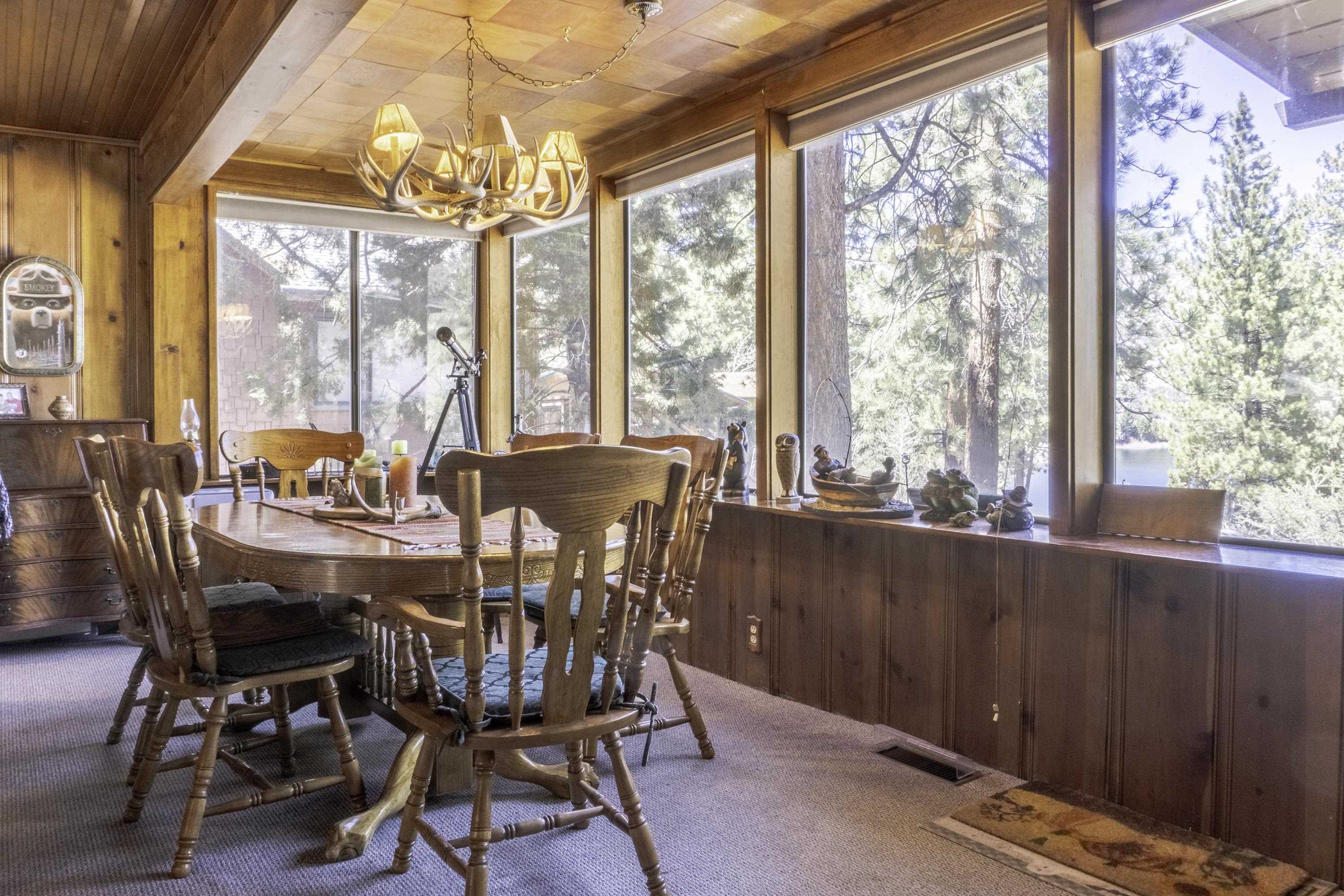 Wood-paneled dining room with an antler chandelier, carved wooden furniture, and lake views through large windows.