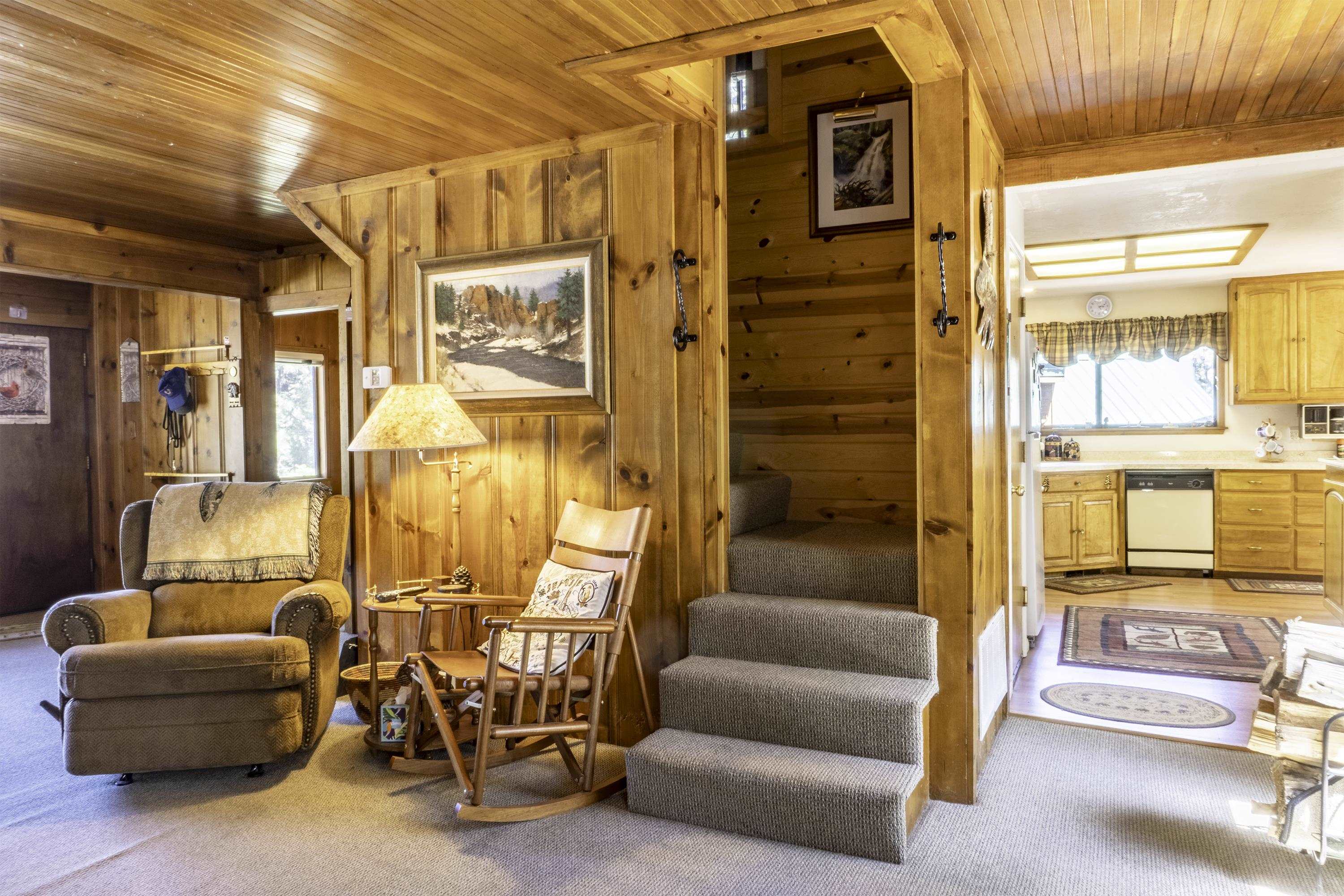 Wood-paneled living room with a recliner, rocking chair, carpeted steps, and adjoining kitchen.