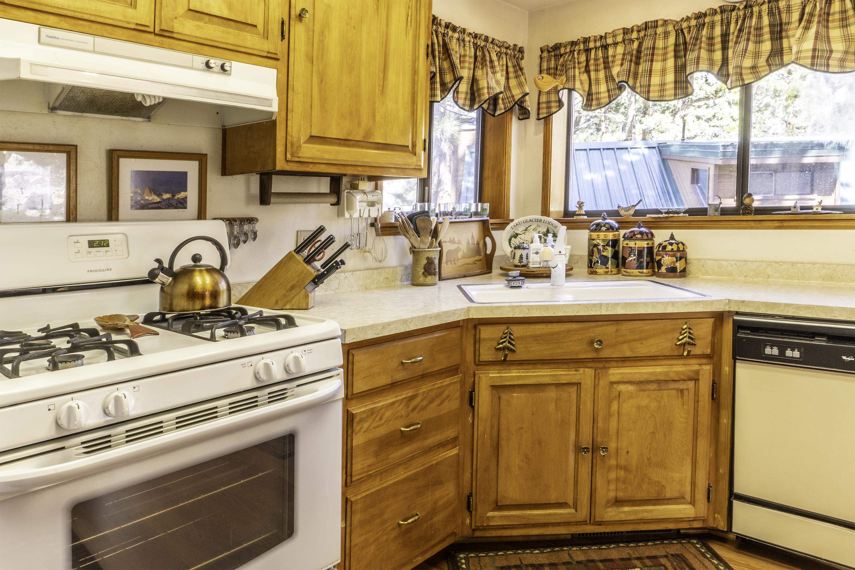 Kitchen with honey-colored wood cabinets, white gas stove, and sink beneath a wide window.