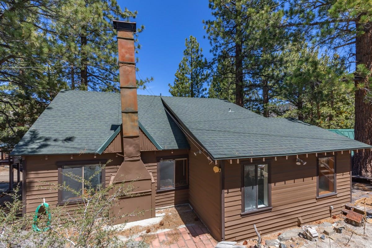 Brown cabin with a tall chimney and green roof among pine trees.