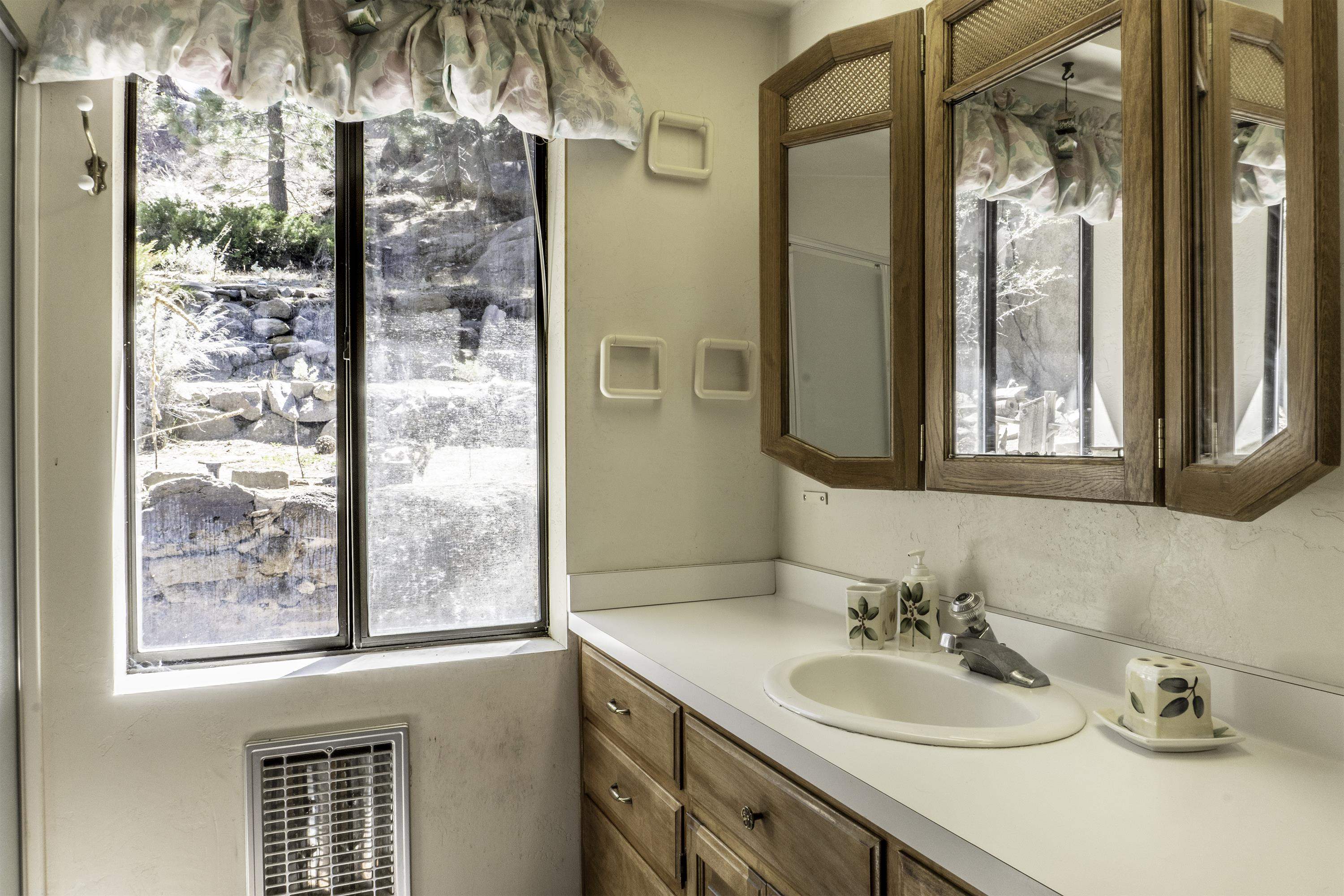 Bathroom vanity with an oval sink, wood-framed mirrored cabinet, and a large window overlooking stone landscaping.