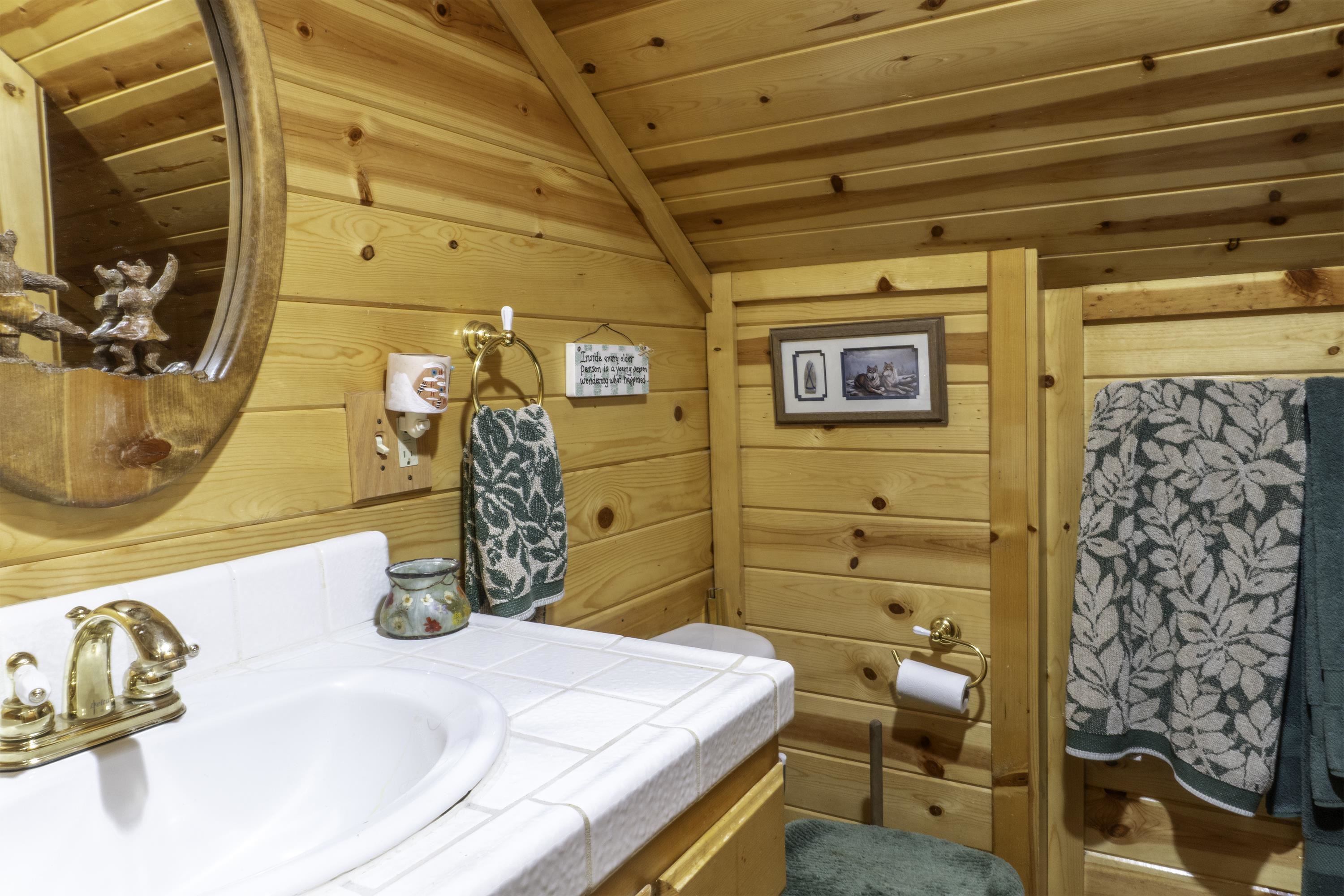 Bathroom with a white tiled sink, honey-toned wood walls, and patterned green towels.