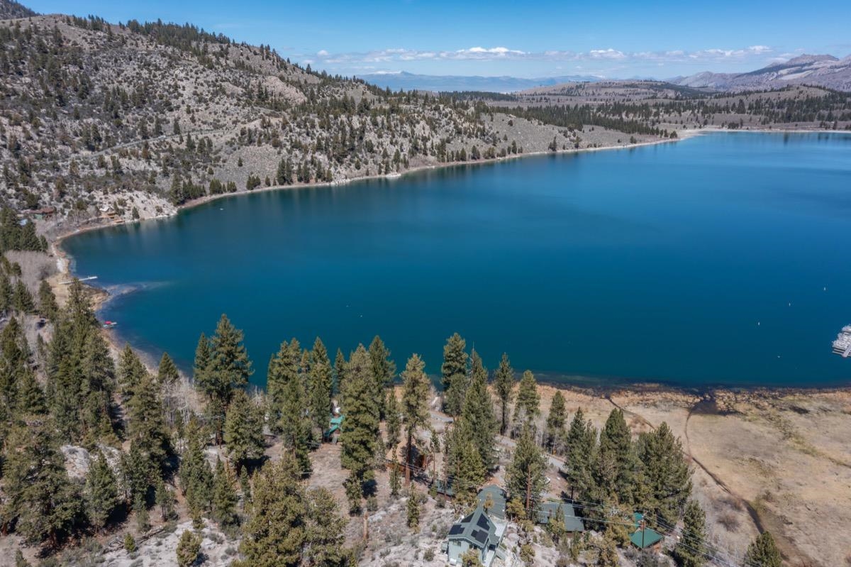 Aerial view of a lakeside home beside a vivid blue lake and wooded mountain shoreline.