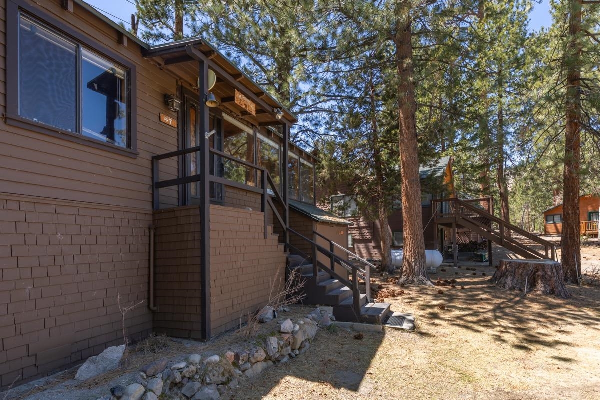 Wood-sided home with a raised entry deck and stairs among tall pine trees.
