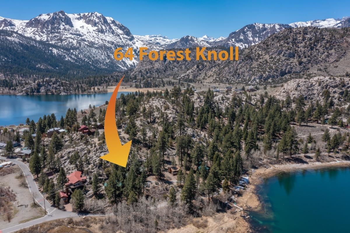 Aerial view of a lakeside home beneath snow-covered mountains, marked by an orange arrow.