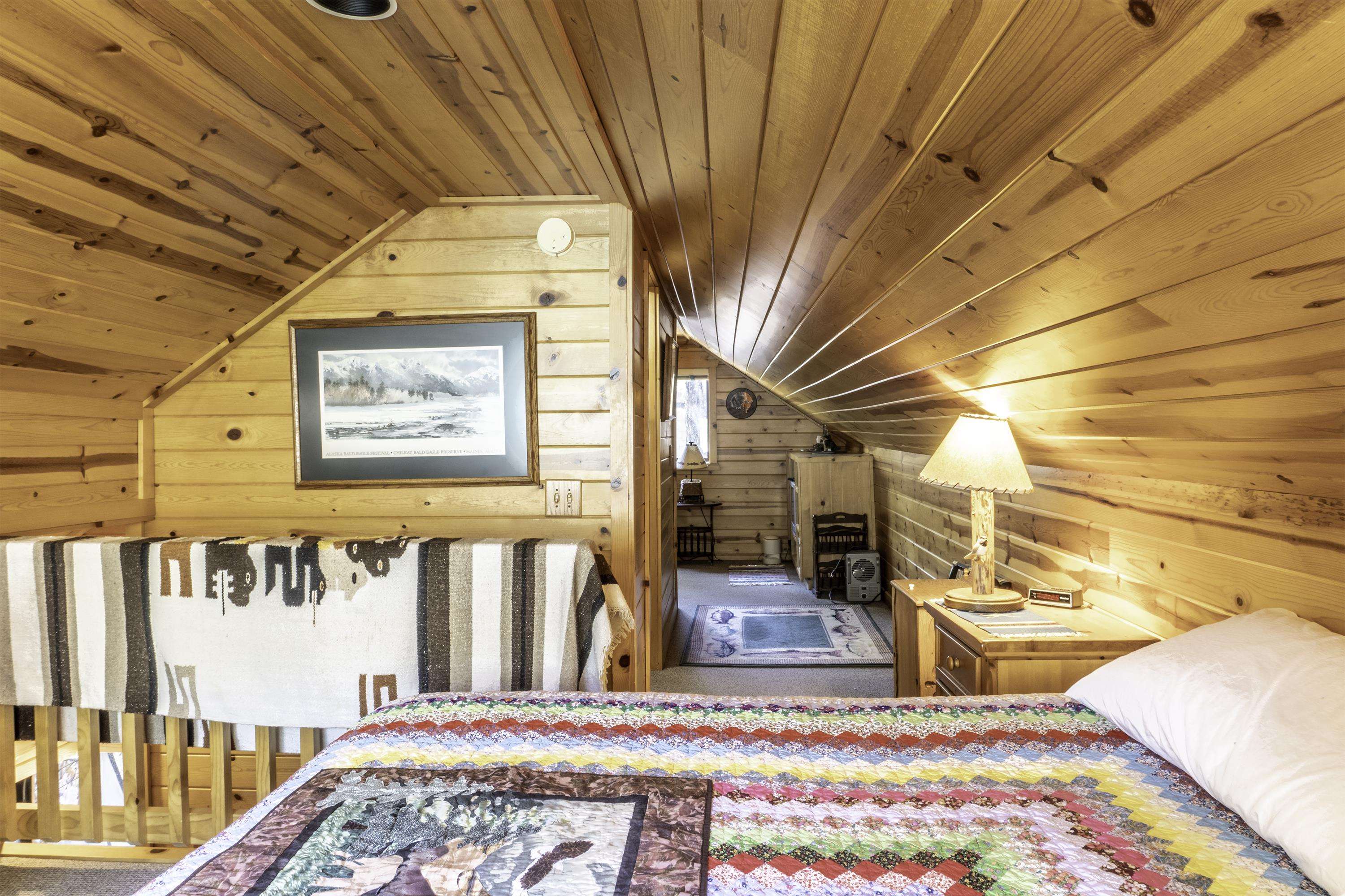 Loft bedroom with a colorful patchwork quilt beneath a sloped, wood-paneled ceiling.