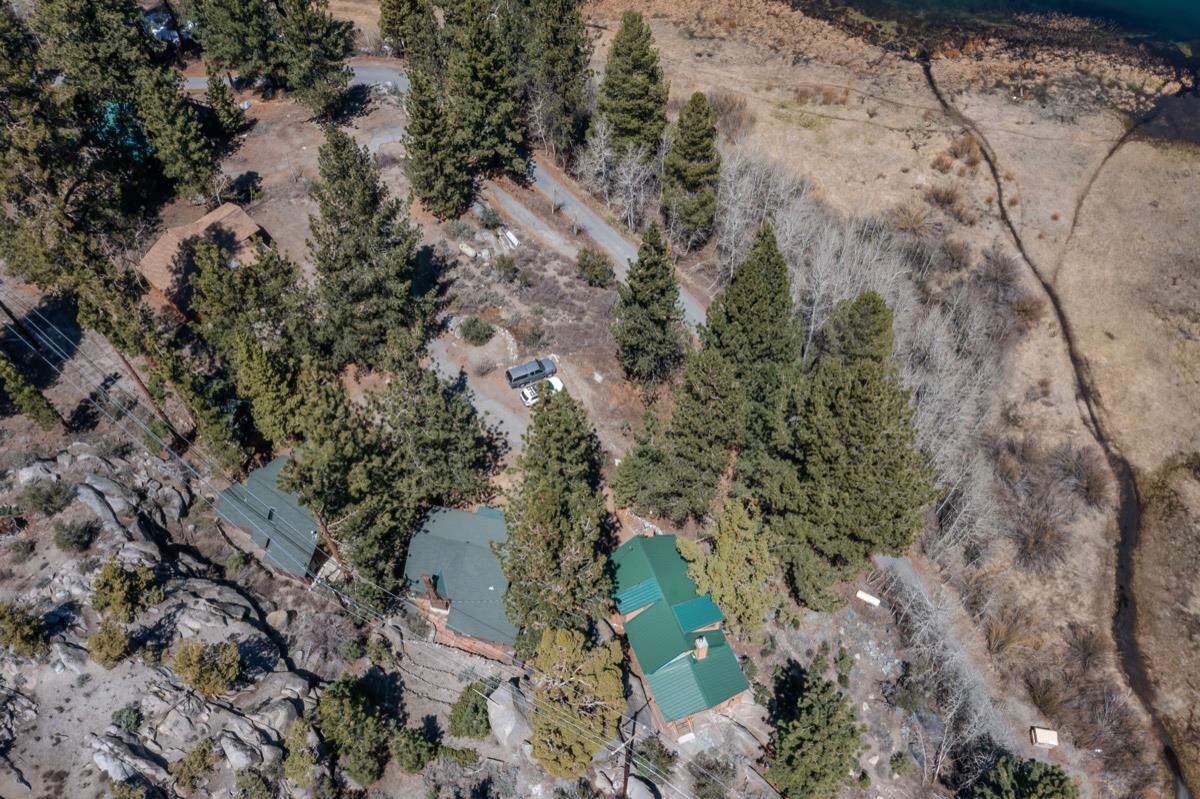 Aerial view of a forested property with green-roofed cabins, rocky terrain, and a winding driveway.