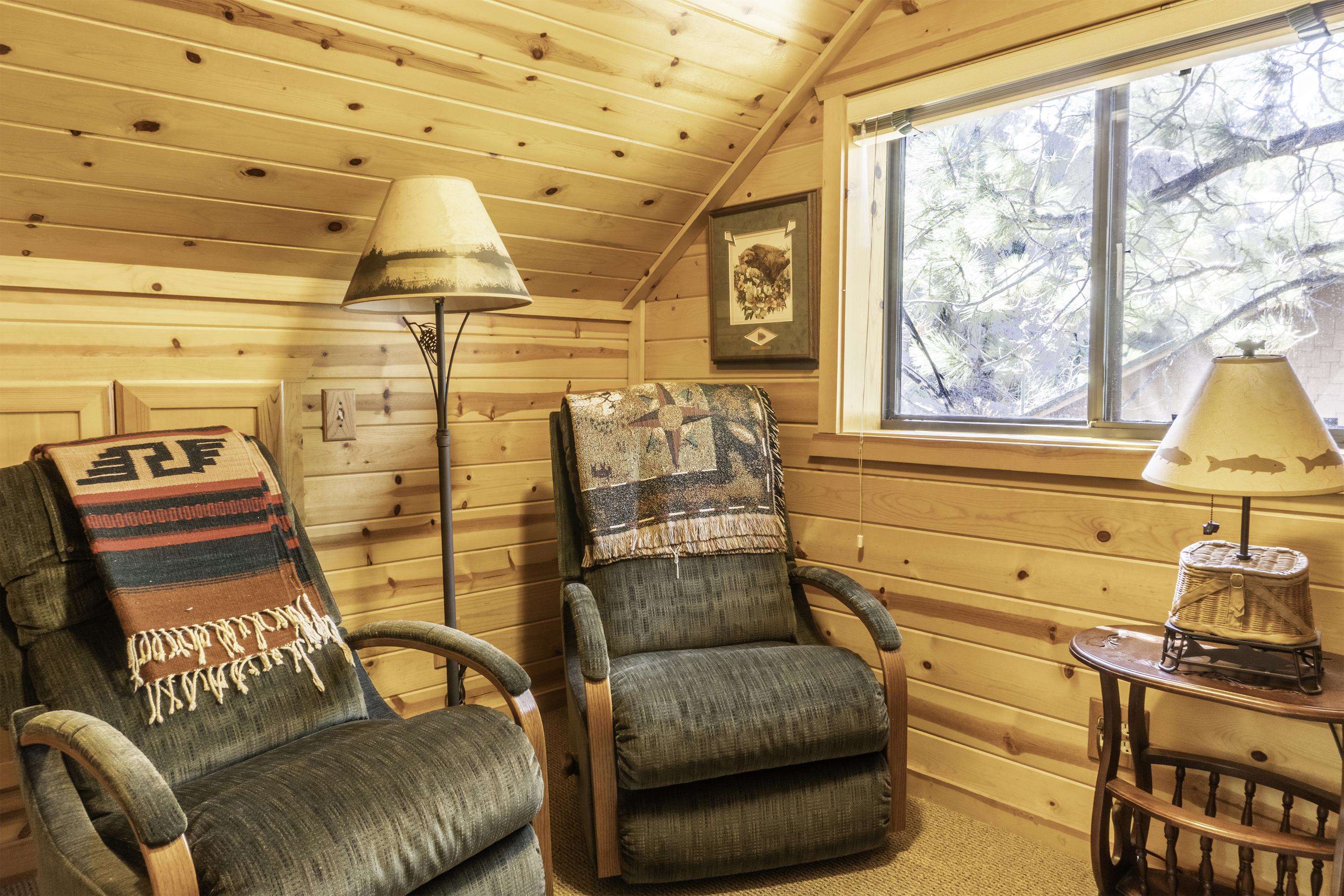 Wood-paneled sitting area with two armchairs, patterned throws, and a large window overlooking trees.