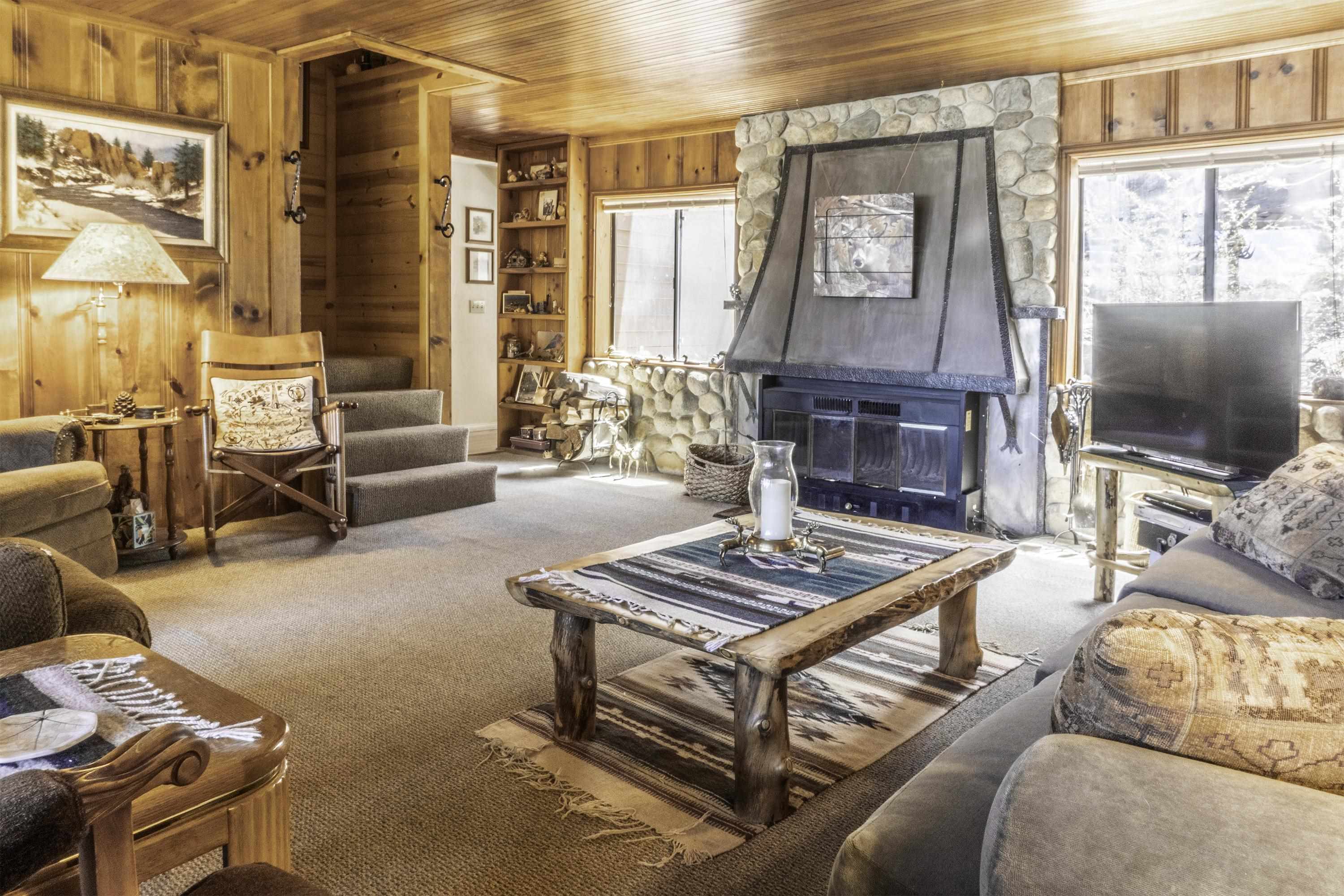 Living room with a stone fireplace, wood-paneled walls, and rustic log coffee table.