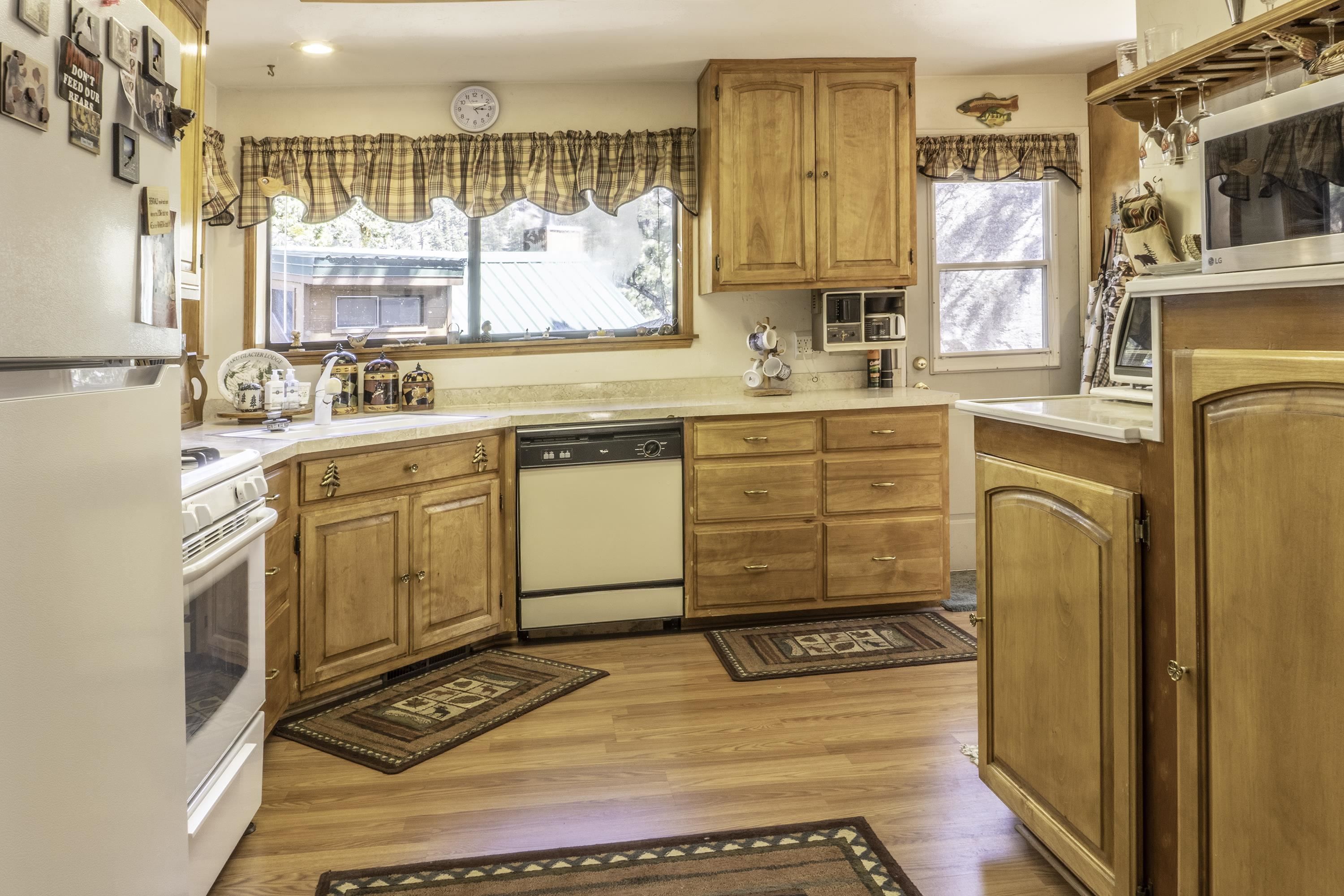 Kitchen with honey-colored wood cabinets, patterned curtains, and a dishwasher beneath the counter.
