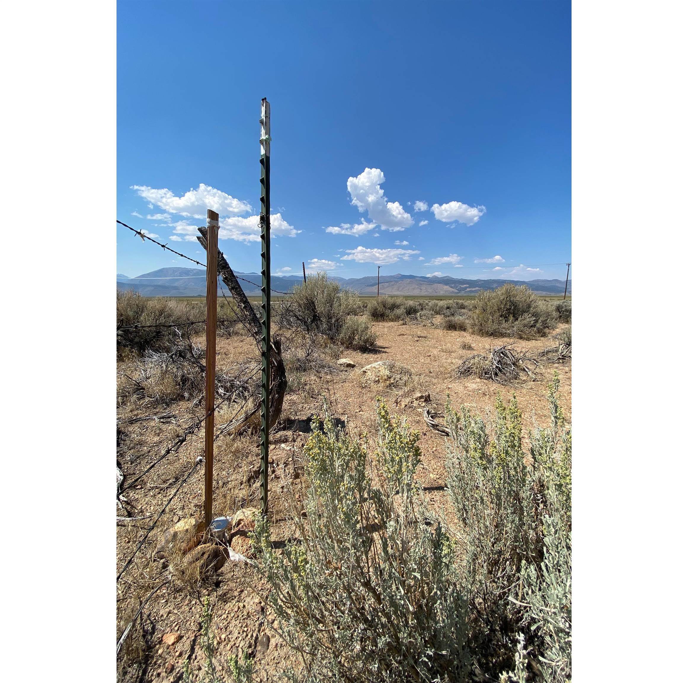 Undeveloped sagebrush parcel with a barbed-wire fence and distant mountain views.