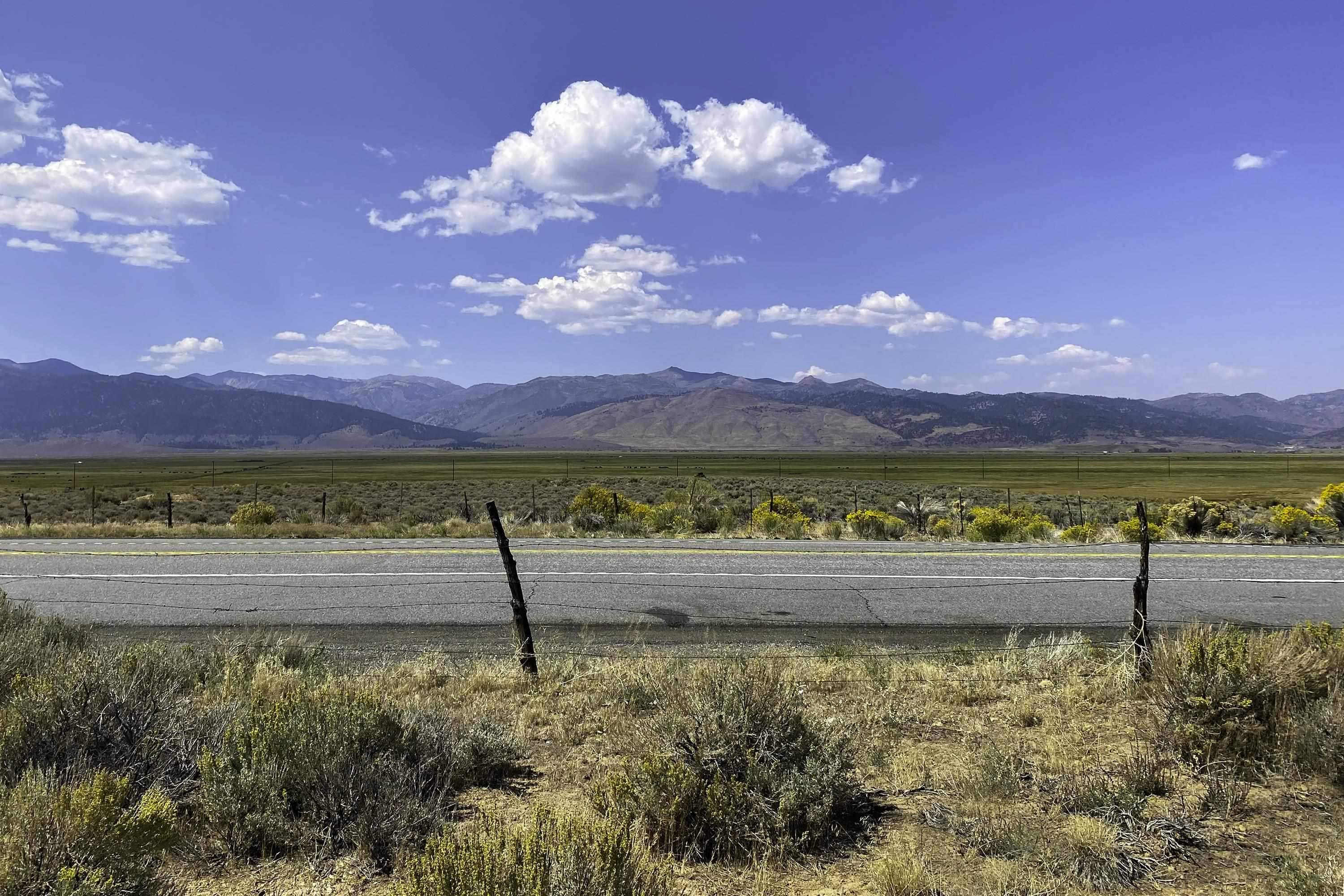Vacant scrubland beside Highway 395, with a wire fence and mountains in the distance.
