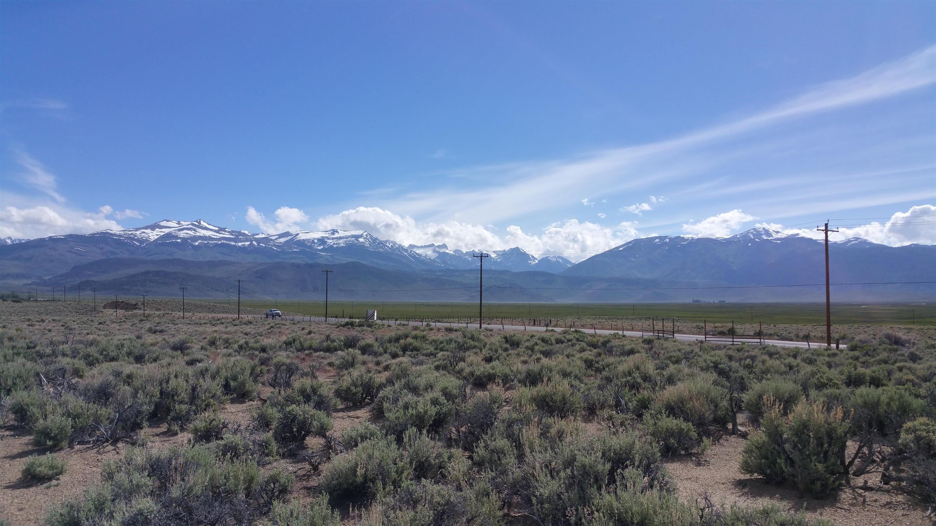 Vacant sagebrush parcel beside a road, with snow-dusted mountains in the distance.