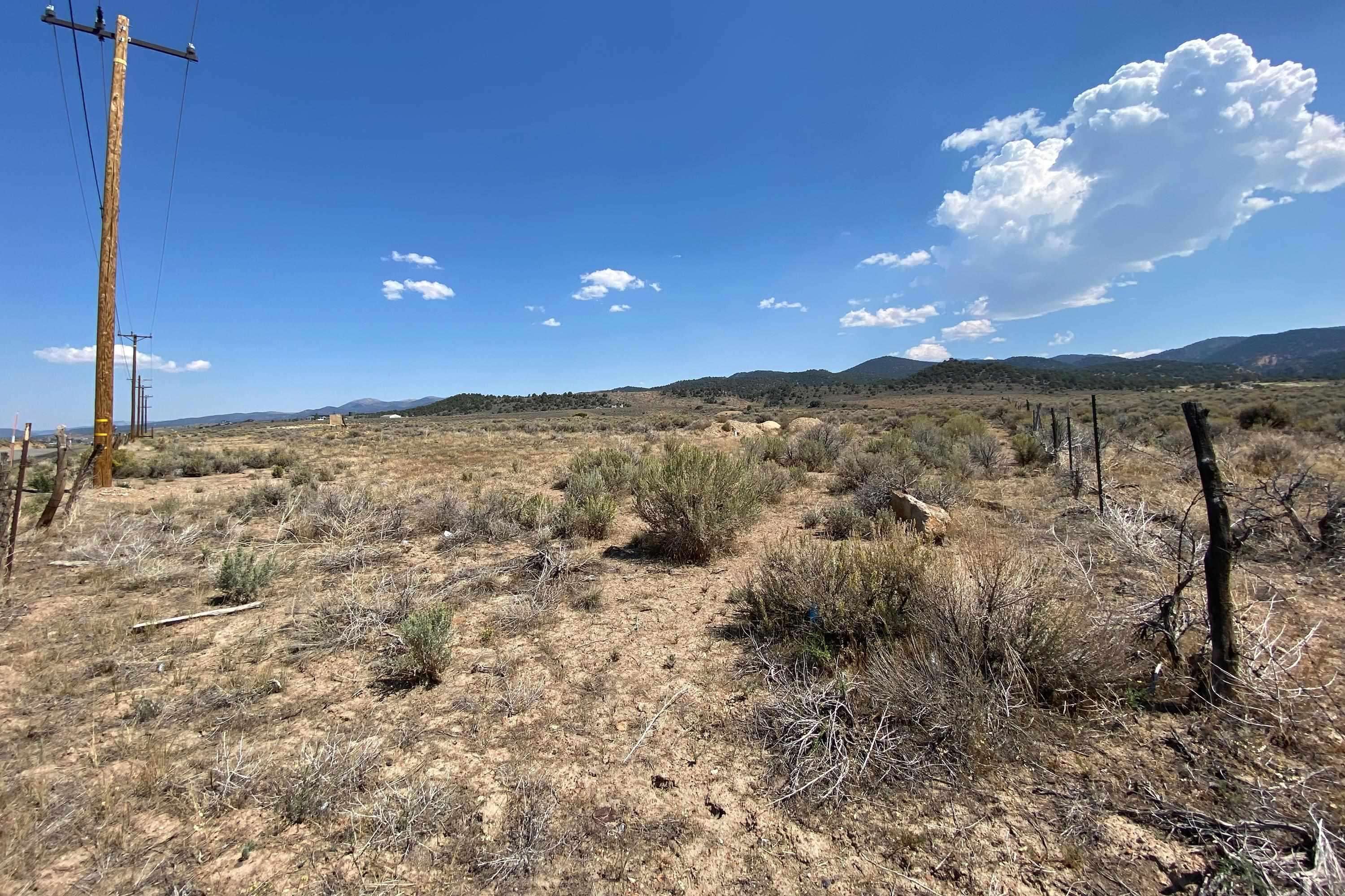 Vacant scrubland parcel with mountain views, utility poles along one side and fence posts along the other.