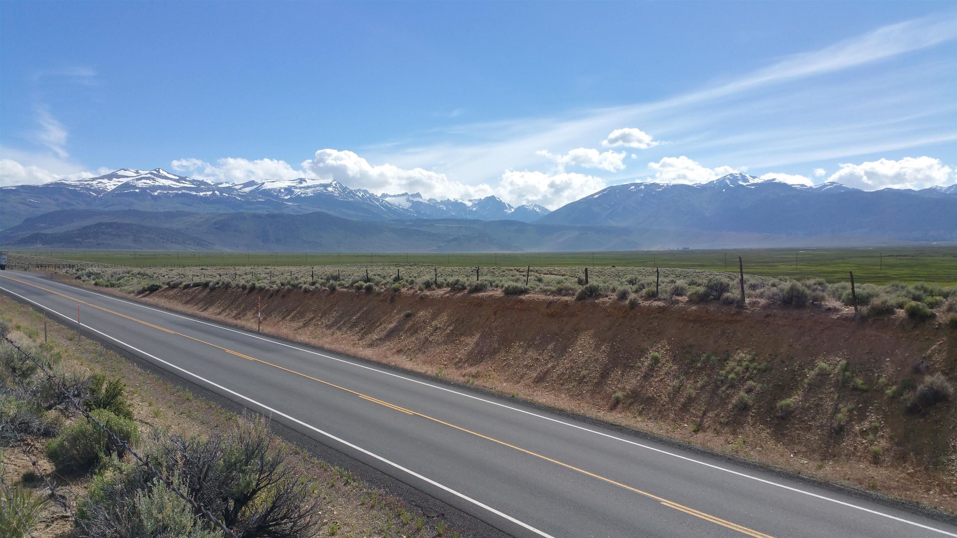Open high-desert land beside a highway, with snow-dusted mountains across the horizon.