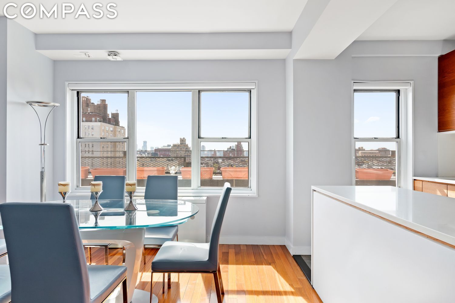Dining area with a glass table, blue chairs, hardwood floors, and city views through large windows.