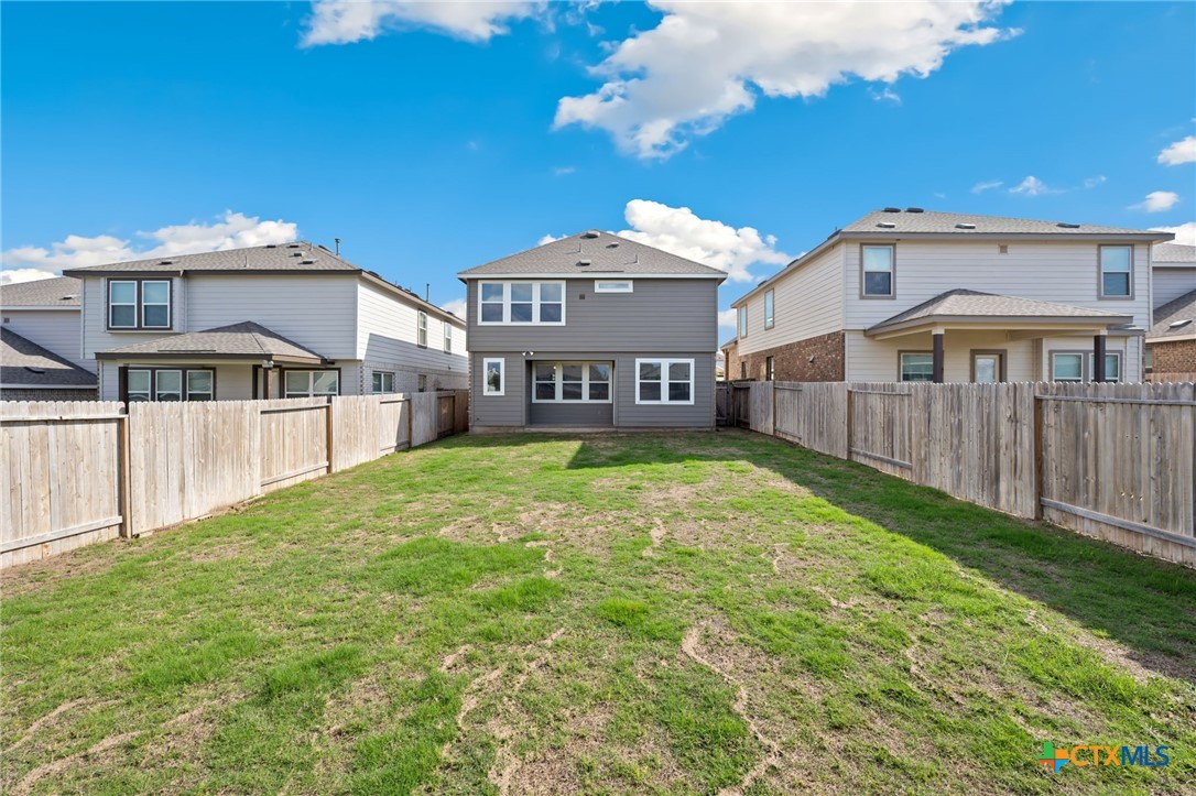 Rear of a two-story gray house with a fenced grassy backyard.
