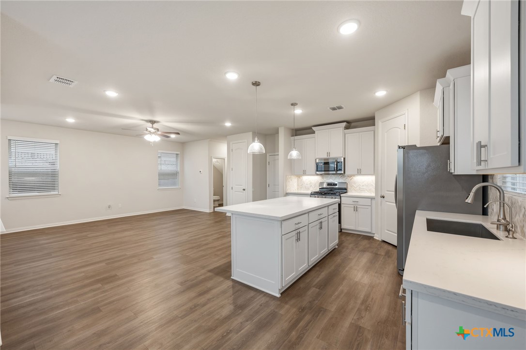 Open-plan kitchen with a large white island, stainless steel appliances, and wood-look flooring.