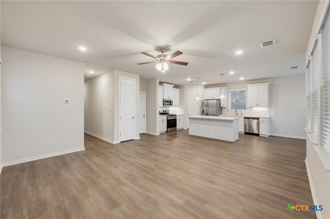 Open-plan kitchen with a white island, stainless steel appliances, and wood-look floors.