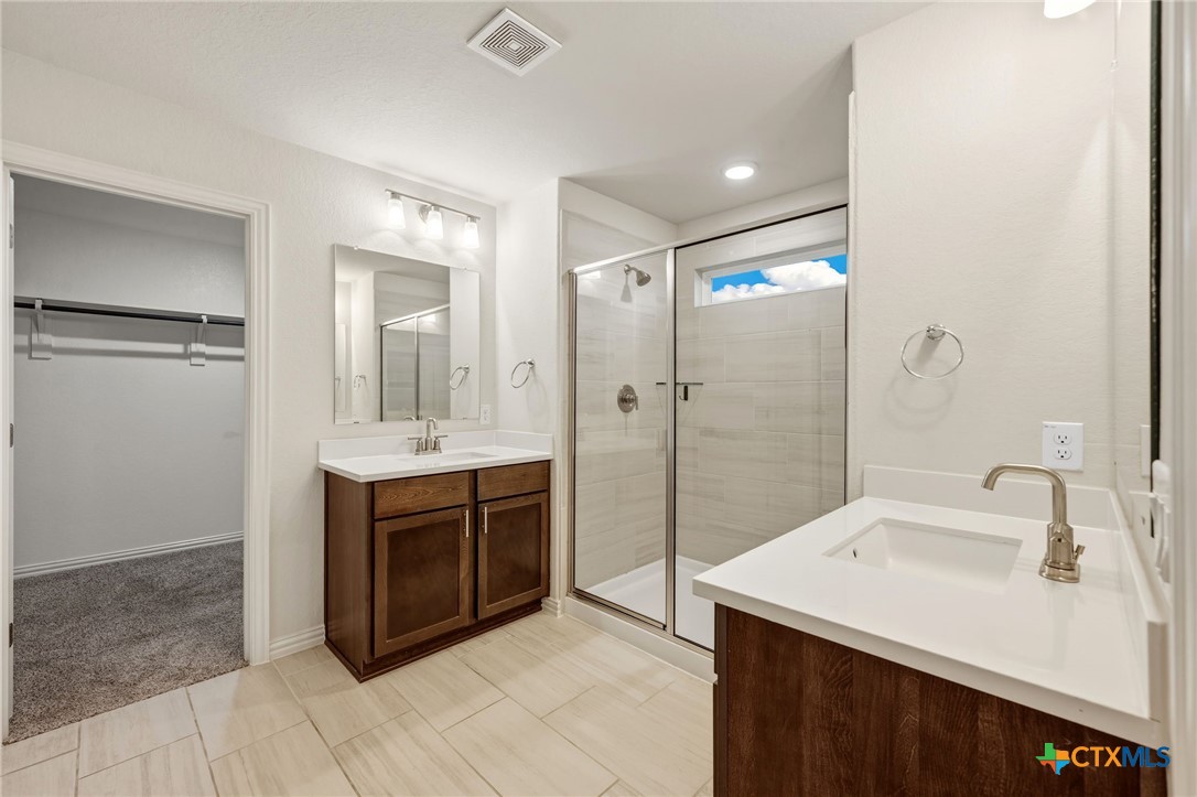 Bathroom with double vanities, a glass shower, and an open doorway to a carpeted closet.