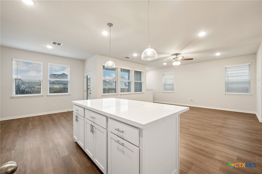 Vacant kitchen with a large white island, wood-look floors, and windows with blinds.
