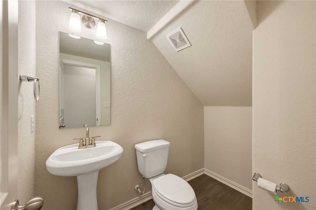 Small bathroom with a pedestal sink and toilet beneath a sloped ceiling.