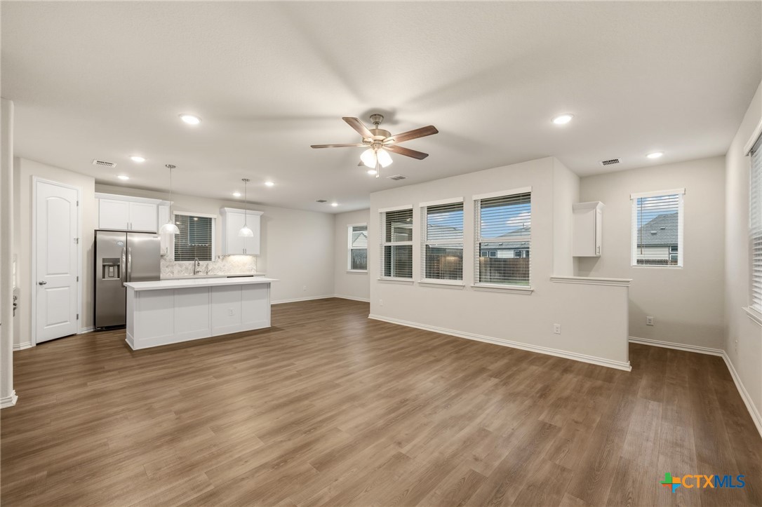 Open-plan kitchen and living area with a white island, stainless steel refrigerator, and wood-look flooring.