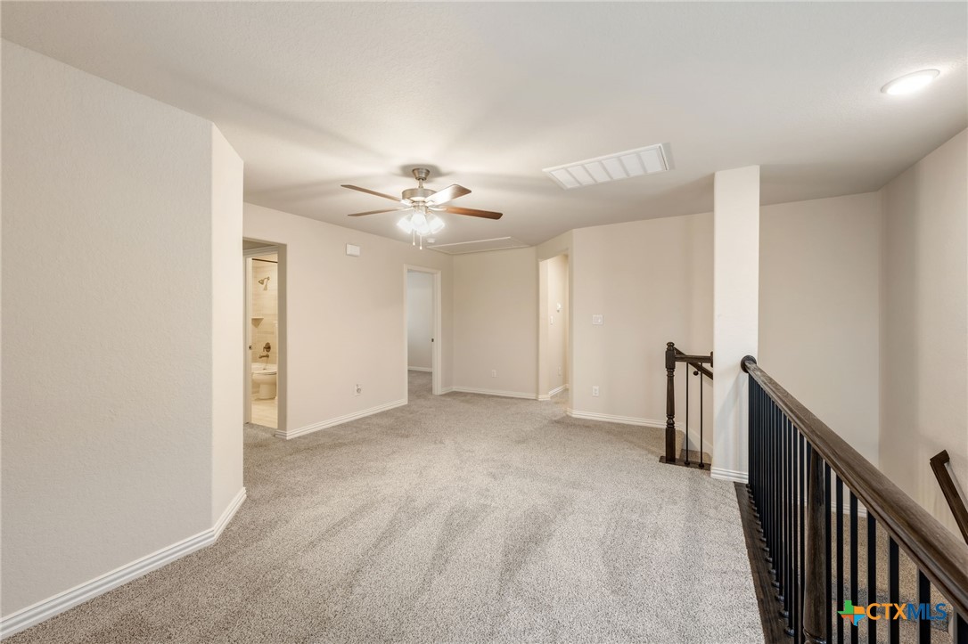 Unfurnished carpeted upstairs landing with a ceiling fan and dark stair railing.