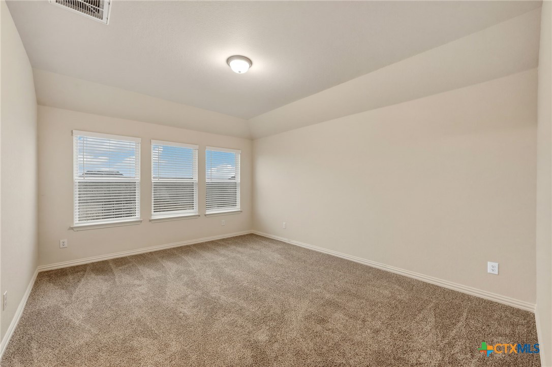 Empty carpeted bedroom with three windows and white blinds.