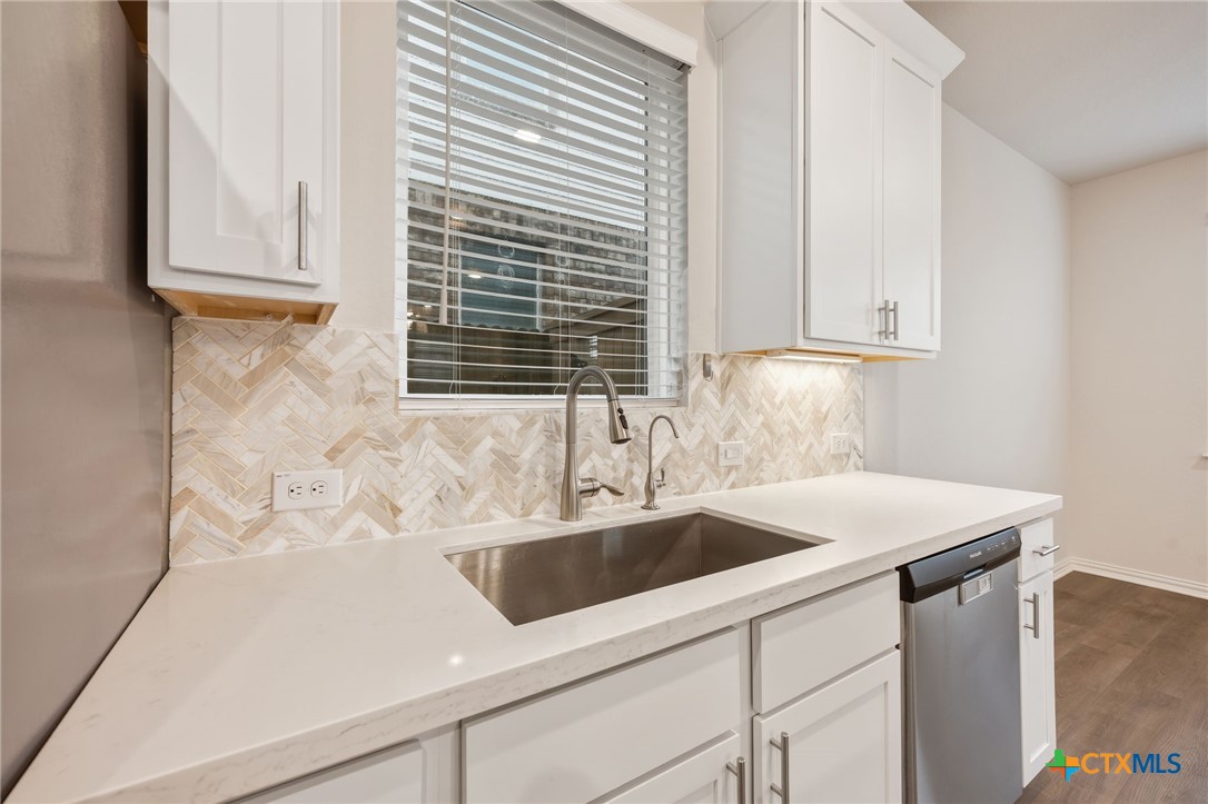 Kitchen with a stainless steel sink, white cabinets, and a pale herringbone backsplash.