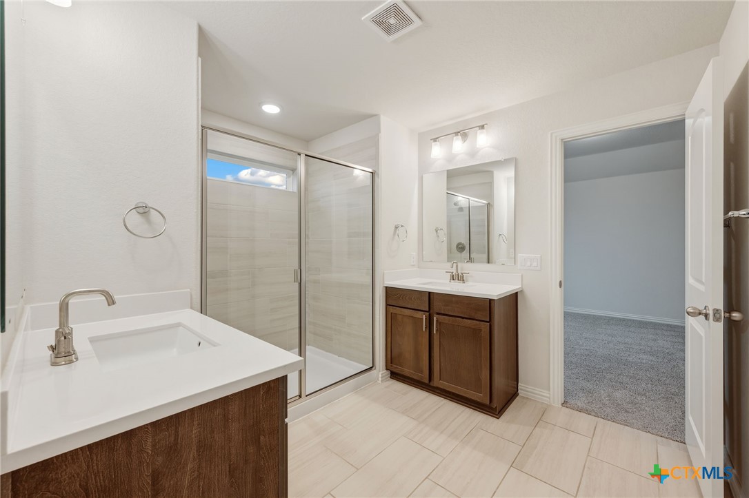 Bathroom with two dark wood vanities, a glass-enclosed shower, and light tile flooring.