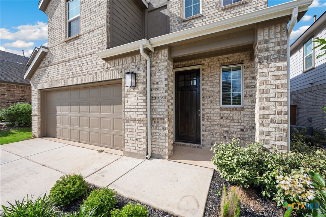 Brick house exterior with a tan double garage door, covered entry, and landscaped shrubs.