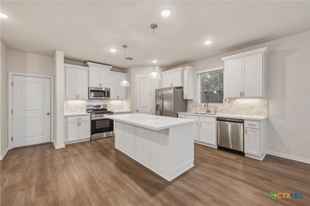 Kitchen with white cabinets, stainless steel appliances, a large island, and wood-look flooring.