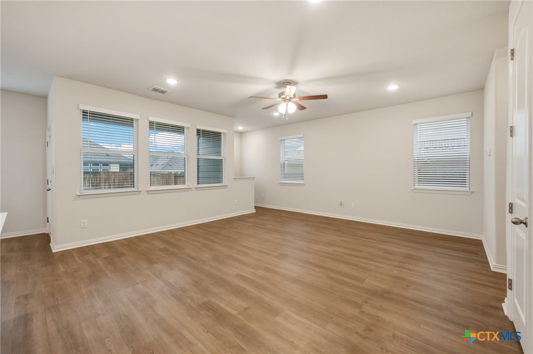 Vacant living room with wood-look flooring, multiple windows, and a ceiling fan.