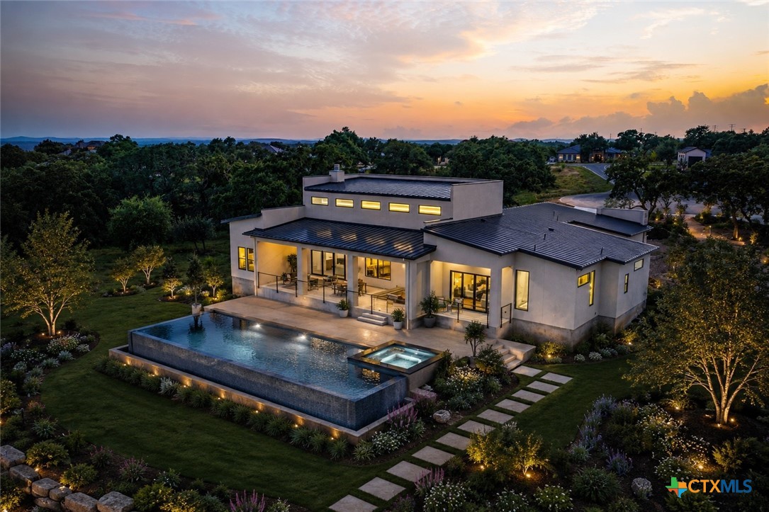 Modern home with a large pool and spa, landscaped garden, and sunset sky.