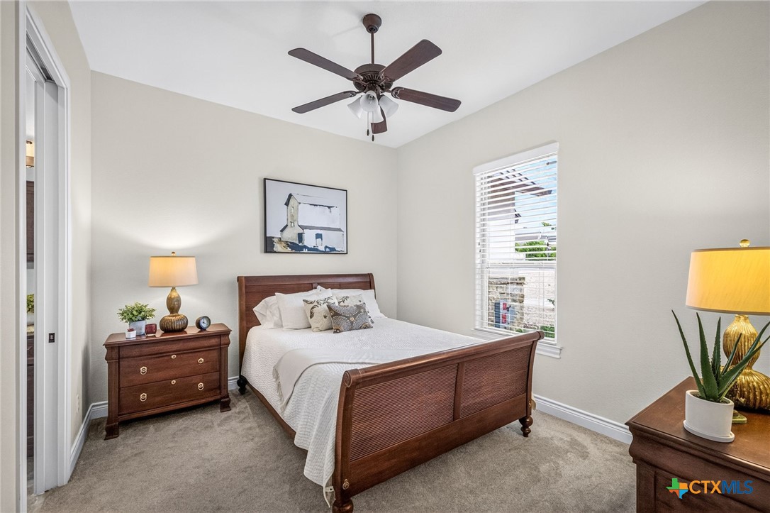 Furnished bedroom with a dark wood bed, white bedding, ceiling fan, and window with blinds.